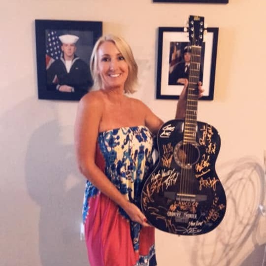 Dawn Spencer holding a Country Thunder acoustic guitar covered in artist signatures.